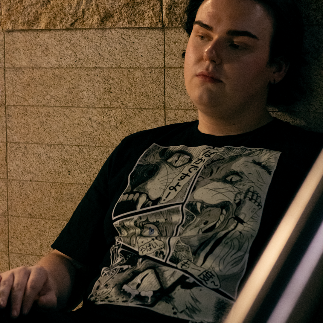 person sitting on ground, back against brick wall, wearing black shirt with 4 panel manga style illustration with japanese text and Therdune logo
