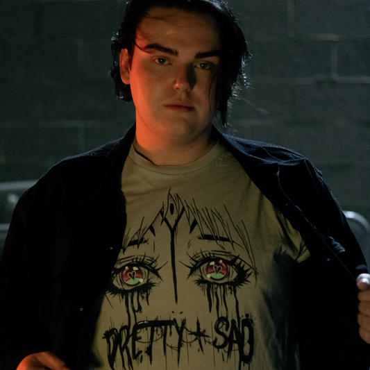 Person wearing a white t-shirt with a graphic print of stylized eyes and the text 'Pretty & Sad' on the front.