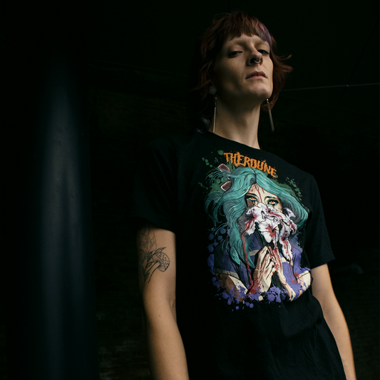 Person wearing a black shirt with anime stylized woman with teal hair holding white flowers dripping blood in front of her face. Orange Therdune logo