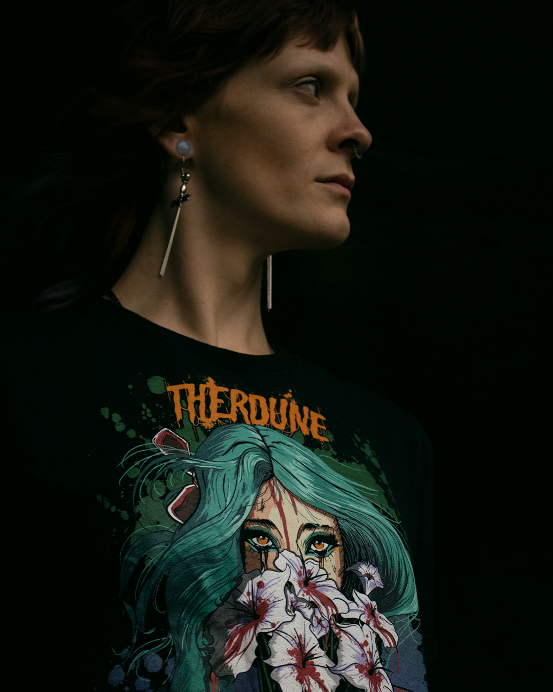 Person looking off in the distance wearing a black shirt with anime stylized woman with teal hair holding white flowers dripping blood in front of her face. Orange Therdune logo