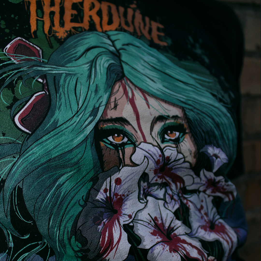 close image of black shirt with anime stylized woman with teal hair holding white flowers dripping blood in front of her face. Orange Therdune logo