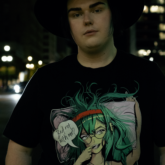 Person in a city wearing black shirt with stylized anime woman with teal hair and bra, speech bubble that says "bed rot with me?"